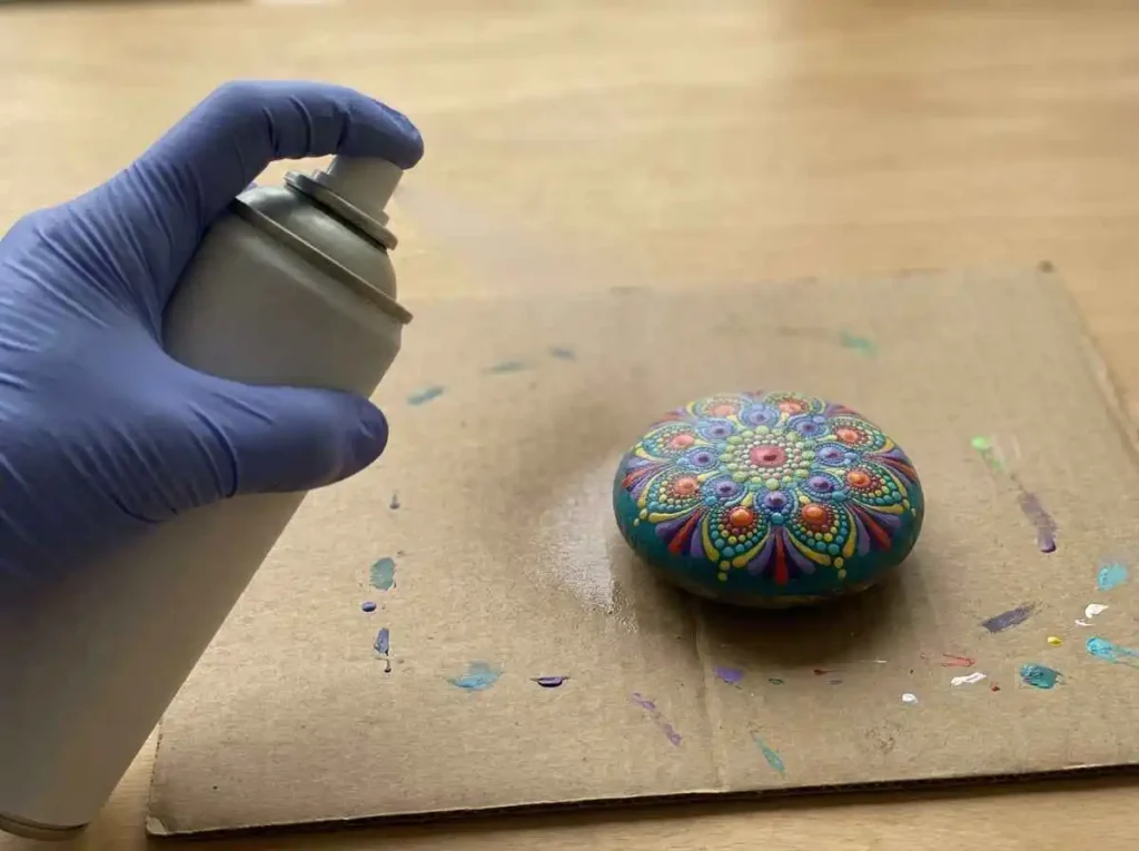 Applying a light even coat of clear sealer to a painted rock