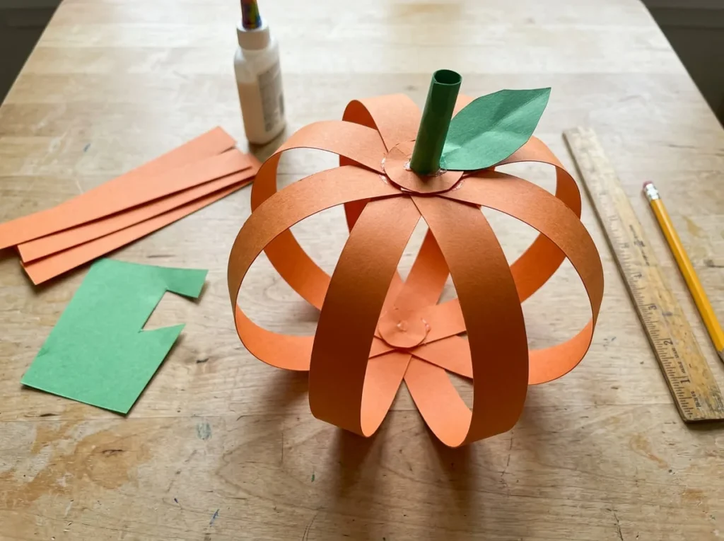 Easy 3D paper pumpkin craft made with curved orange cardstock strips and a green stem