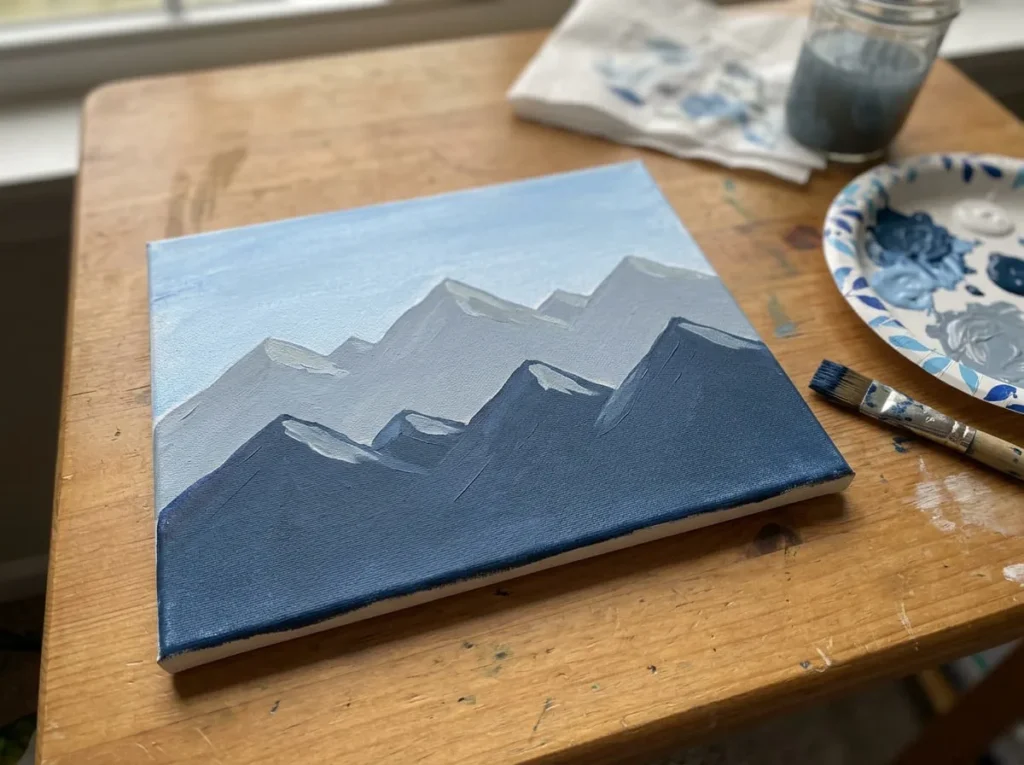 Beginner acrylic mountain painting with pale blue sky and two overlapping layers of blue-gray mountains.