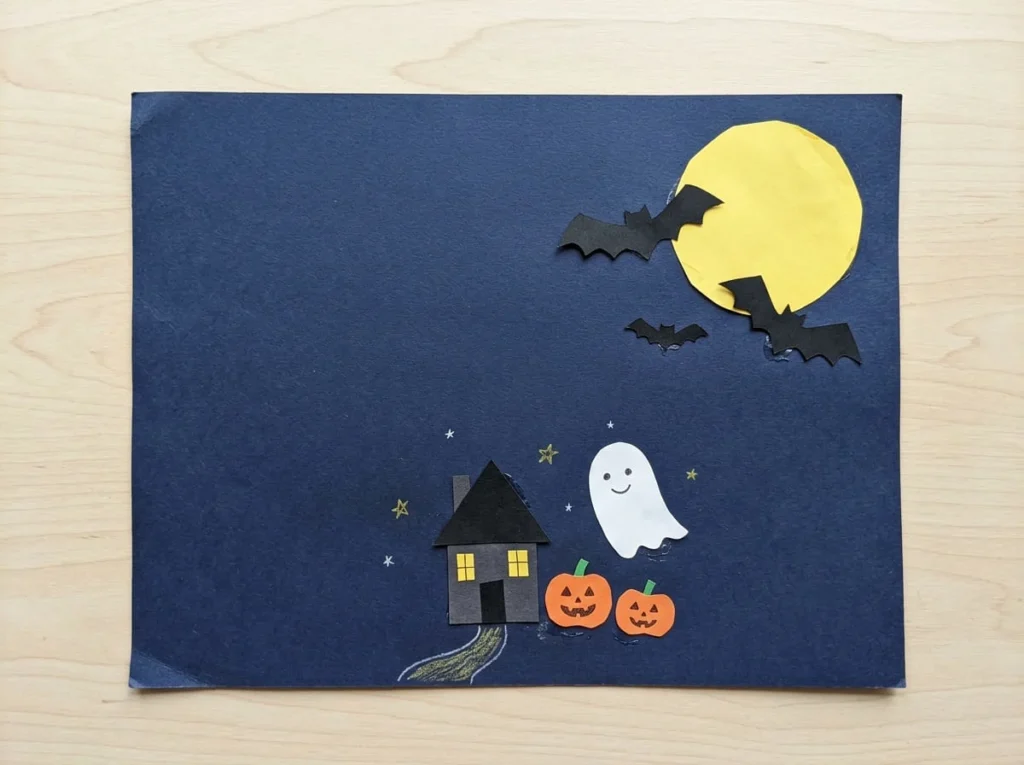 Halloween paper scene collage with a moon, bats, pumpkins, a house, and a friendly ghost