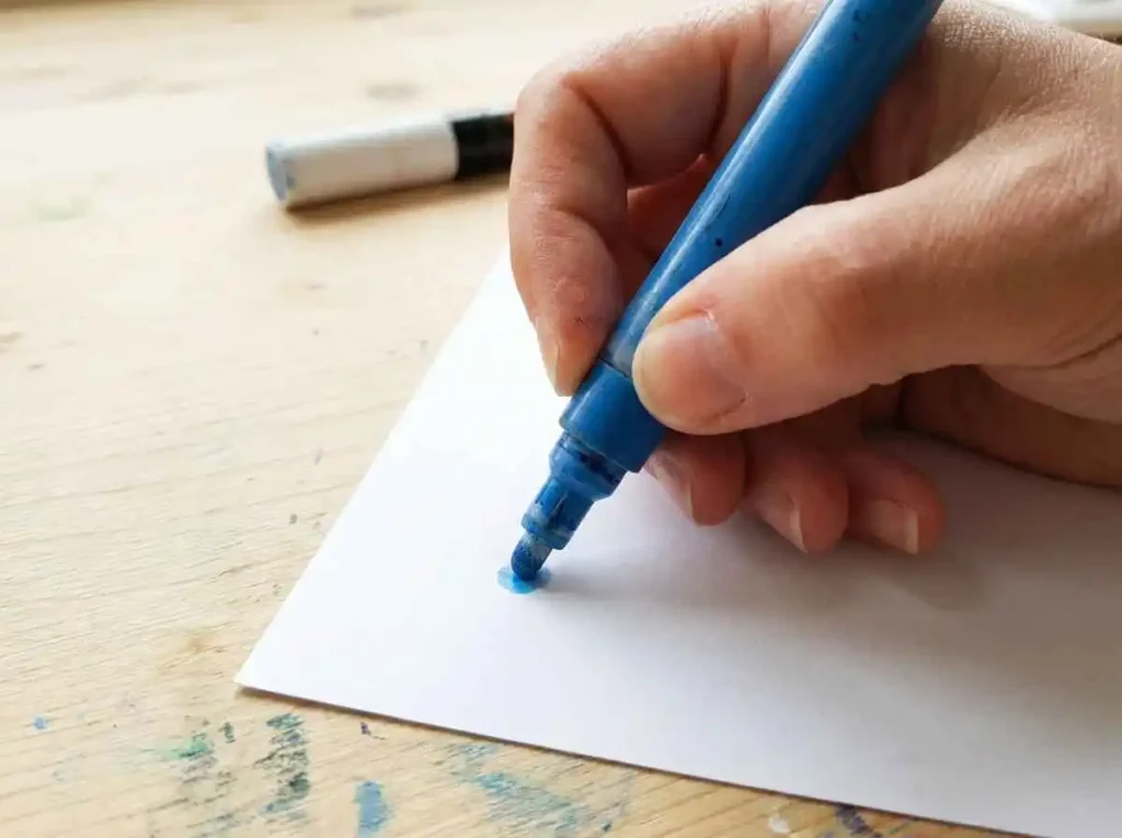 Close-up of a hand gently priming a pump-action acrylic paint pen on scrap paper.