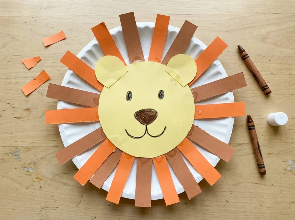 Handmade paper plate lion face with an orange paper mane, rounded ears, and simple crayon features.